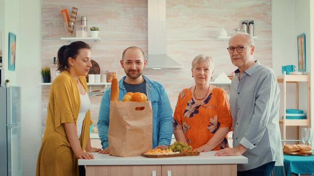 Slow motion video family portrait sitting in the modern kitchen. Happy people smiling at the camera in dining room around the papper bag with groceries looking at the camera