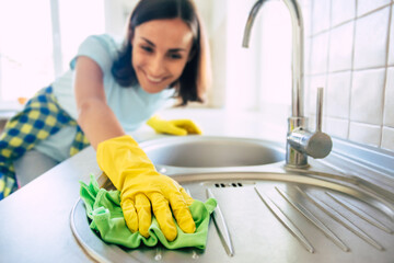 Young happy cute woman in yellow gloves is cleaning her kitchen at home
