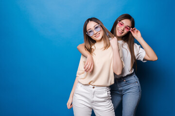 Friends forever. Two cute lovely girl friends in sunglasses posing with smile isolated on blue...