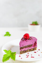 A slice of blackcurrant mousse cashew cake and chocolate praline on a white plate. Sugar, lactose, gluten free. Vegan dessert, healthy food.