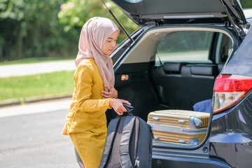 Businesswoman on a business travel  putting suitcase in car trunk.