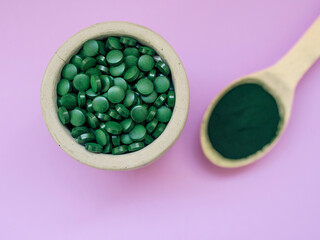 Green hawaiian spirulina in tablespoons pills and powder on light lilac background. Super food, healthy lifestyle, healthy supplements concept