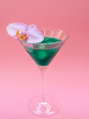 Liquid spirulina green drink with Phalaenopsis in cocktail glass on pink background. Super food, healthy lifestyle, healthy supplements concept