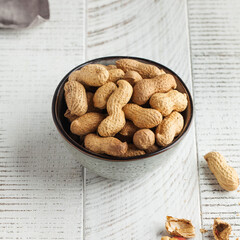 Peanuts in a shell in a gray bowl on a white wooden background. Healthy snacks, vegetable fats.