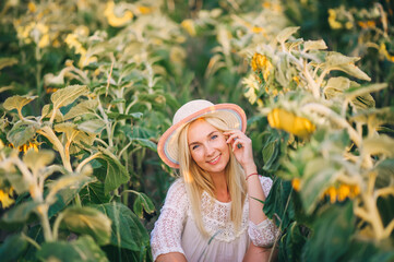 Portrait of a young blonde woman in white blouse sitting on a background sunflowers