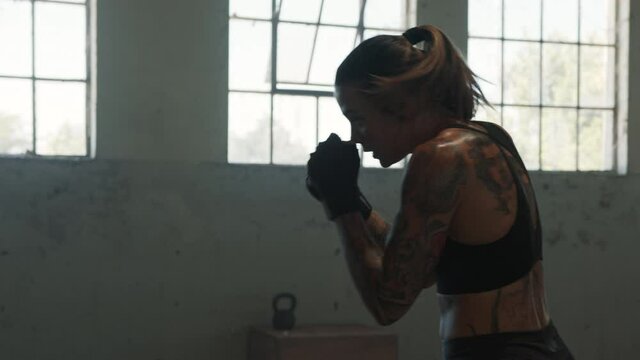 Fitness female practising shadow boxing in cross training workout space. Sportswoman exercising in gym, working out on her boxing moves.
