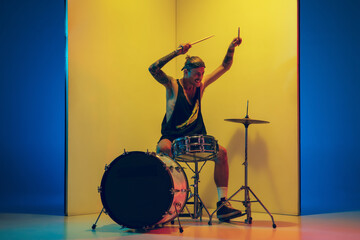 Fototapeta na wymiar Youth. Young musician with drums performing on yellow background in neon light. Concept of music, hobby, festival, entertainment, emotions. Joyful, inspired drummer. Colorful portrait of artist.
