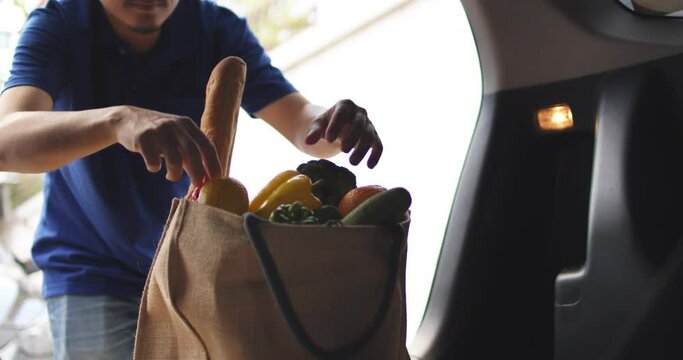 A courier delivery man holding food and vegetables from car to home of customer. Working in a pandemic during covid 19 or coronavirus