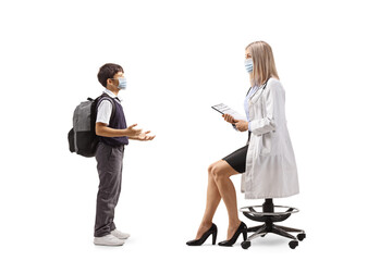 Obraz premium Schoolboy in a uniform with a face mask talking to a female doctor seated on a chair