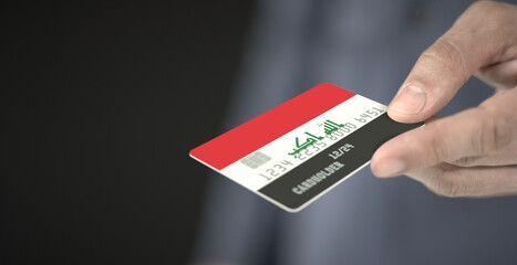 Man gives plastic bank card with printed flag of Iraq. Fictional numbers