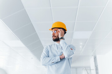 Portrait of engineer in white clothes and orange protective hard hat that standing and working indoors
