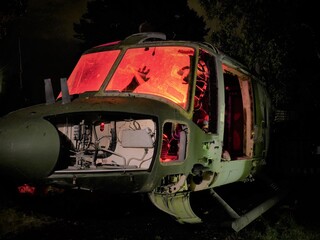 disused abandoned Helicopter grounded at night with red internal lighting to show hand silhouette, nose body and component parts 