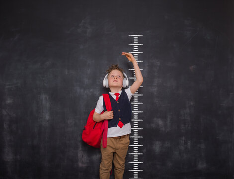 Little kid boy measuring himself. School boy measuring his growth in height against a blackboard scale. Back to school