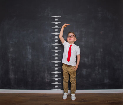 Little kid boy measuring himself. School boy measuring his growth in height against a blackboard scale. Back to school. Ready to go to school