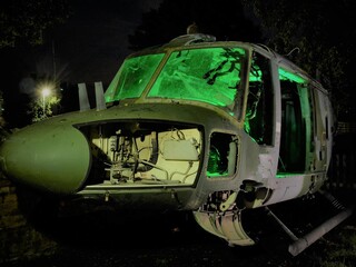 disused abandoned Helicopter grounded at night with green lighting to show nose body component parts and lit windows