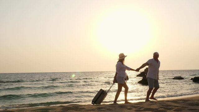 Romantic couple of lovers, silhouettes. travelers walk along the beach, holding hands, with travel suitcase against backdrop of sea, sunrise or sunset. travel concept. Honeymoon. seaside vacation