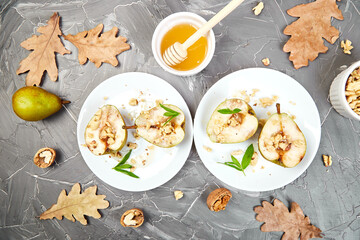Tasty roast pears with honey and walnuts on white plates on grey background table.
