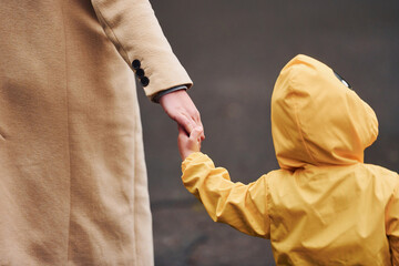 Kid in yellow waterproof cloak holding mother's hand and have a walk outdoors