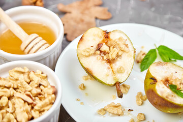 Tasty roast pears with honey and walnuts on white plates on grey background table.