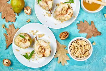 Tasty roast pears with honey and walnuts on blue background table.