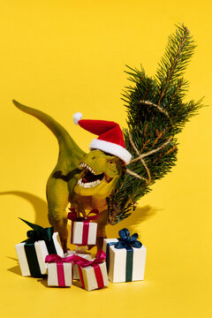 Decorative dinosaur in Christmas hat holding fir and presents