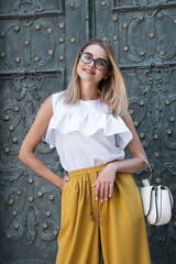 Young elegant girl posing at city street. Pretty beautiful business woman in elegant white sundress and yellow pants