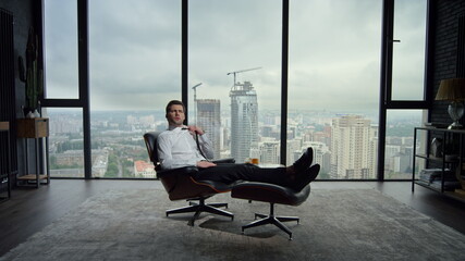 Businessman sitting on chair in modern interior. Professional adjusting tie