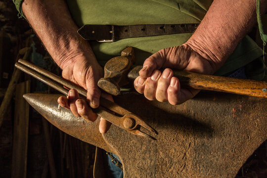 A farrier's hands clasped above an anvil