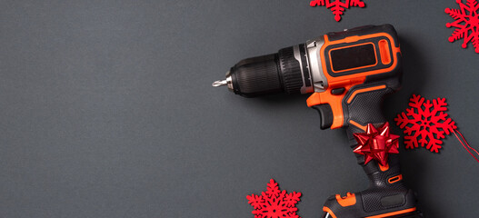 Christmas background with tool. Electric screwdriver and Christmas decorations on a black background top view, copy space. Free space for text. Christmas sale of construction tools.