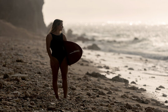 Young woman holding surfboard on an empty beach, Bali