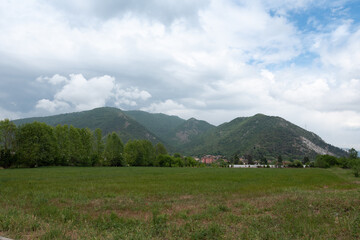 Obraz premium Field with green grass on a background of mountains and cloudy sky. Let's save the world.