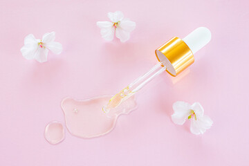 Cosmetic pipette with oil on pink background close-up. Around - white flowers. Stylish concept of organic essences, beauty and health products. Copy space, minimalism, flat lay. Modern apothecary.