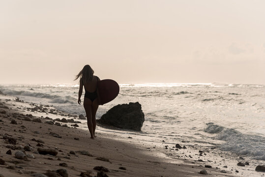 Silhouette of young woman holding surfboard on an empty beach, Bali