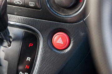 Close-up of an emergency button with a white triangle icon on the red plastic of a car dashboard. Signal of breakage, problem, or accident and damage.