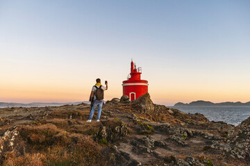 taking a picture with an iPhone of a red lighthouse on the coast, near the sea.