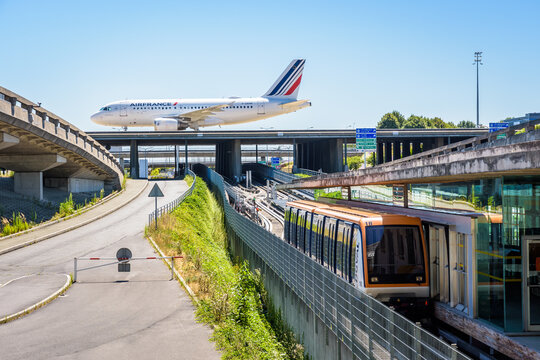 Roissy-en-France, France - July 27, 2020: An Air France airliner is rolling on a taxiway bridge of Paris-Charles de Gaulle Airport as a CDGVAL airport shuttle is stationing at the Terminal 1 station.
