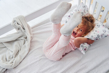 Lying down on the bed. Cute little girl in casual clothes is indoors at home at daytime