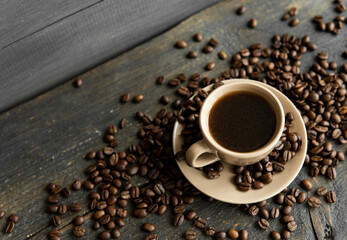Coffee cup with roasted coffee beans on wooden table background. Mug of black coffe with scattered coffee beans on a wooden table. Fresh coffee beans.