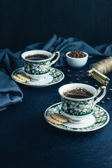 Two cups of brewed black coffee with tea biscuits.