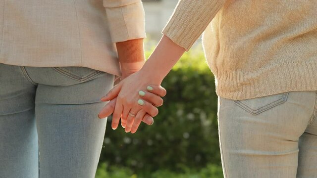 Close-up of hands joining together with sunlight flare in the background. Woman doing first step to make up a quarrel and take hand of her girfriend. Female couple. LGBT Pride Month, Gay Pride Symbol