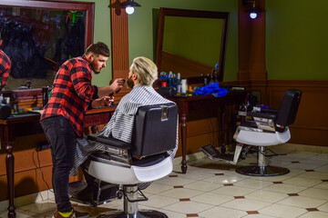 Concept Barbershop. Young hipster man with beard cutting his hair in a barbershop. Professional...