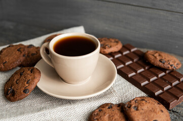 Coffee cup with cookies and chocolate on wooden table background. Mug of black coffee with chocolate cookies. Fresh coffee beans.