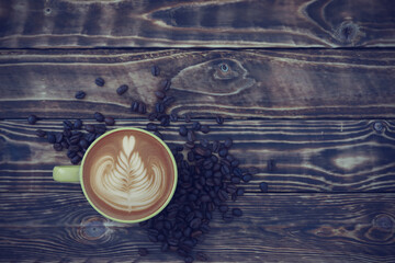 Top view, flat lay latte art coffee in a yellow cup with coffee beans on the old wooden table background.