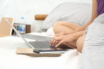 Womans sitting on bed in bedroom working with computer.