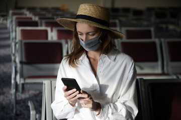 Tourist woman traveling with mask and using phone at the airport. Safety measures during coronavirus. New normal concept. 