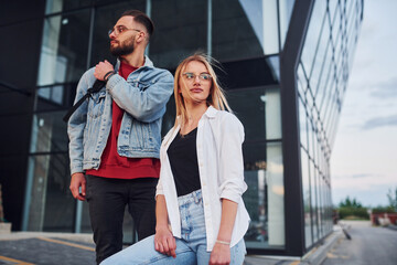 Young stylish man with woman in casual clothes outdoors together near business building. Conception of friendship or relationships