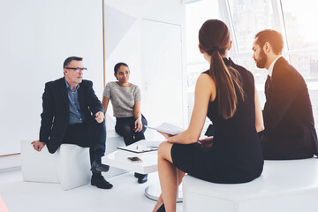 Back view of female lawyer holding documentation consulting owners of trading corporation.Matured male CEO listening to ideas and opinions of professional employees during conference in modern office
