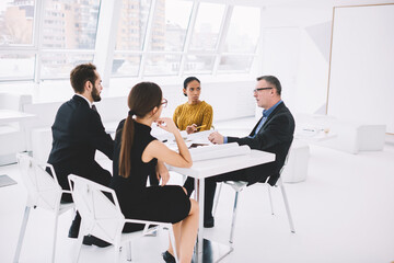Employees of marketing corporation discussing working plans of meeting table in loft office.Proud male CEO communicating with professional colleagues explaining information during conference