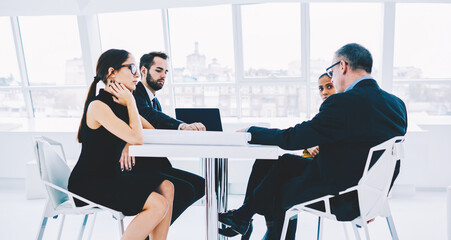 Group of male and female business experts sitting at meeting table discussing collaboration details, young managers consulting with CEO about working process solving problems together in office