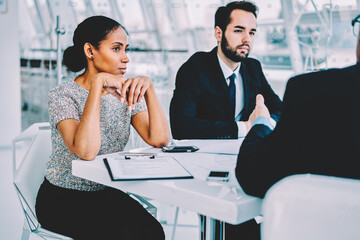 Professional afro american businesswoman analyzing information during meeting with investors sitting with colleague at conference, skilled lawyers discussing details and pondering on solutions